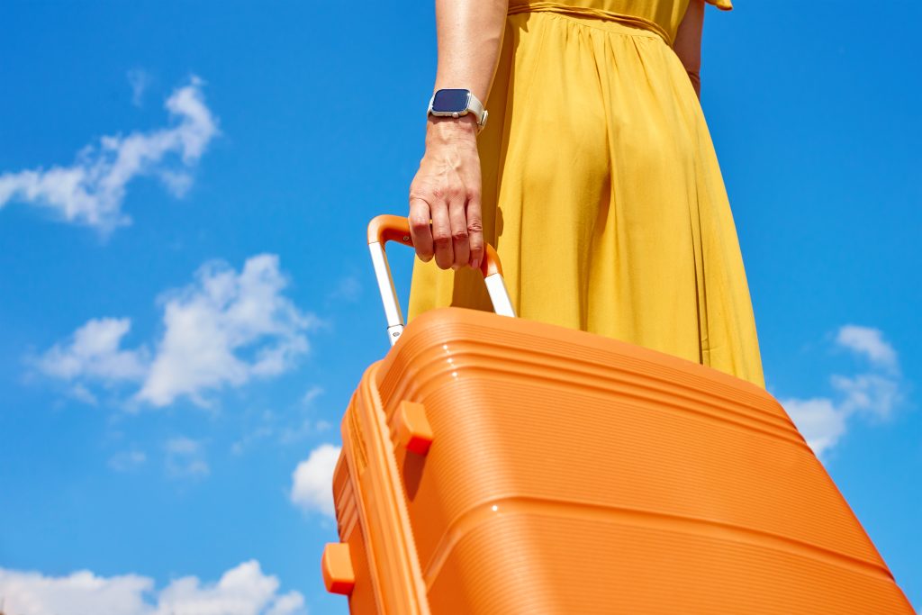 WomanInYellowDressHoldingAnOrangeSuitcaseAgainstBlue | クロスボーダーネクスト株式会社