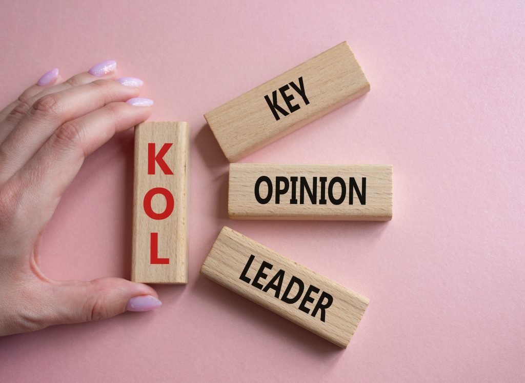 Hand placing wooden blocks spelling KEY, OPTION, LEADER on a pink background, illustrating choices and leadership concepts.