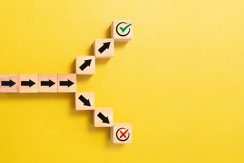 Wooden blocks form an ascending staircase with black right arrows; the top block shows a green check, the bottom shows a red X on a yellow background, conveying progress/approval. You can use this as a progress indicator.
